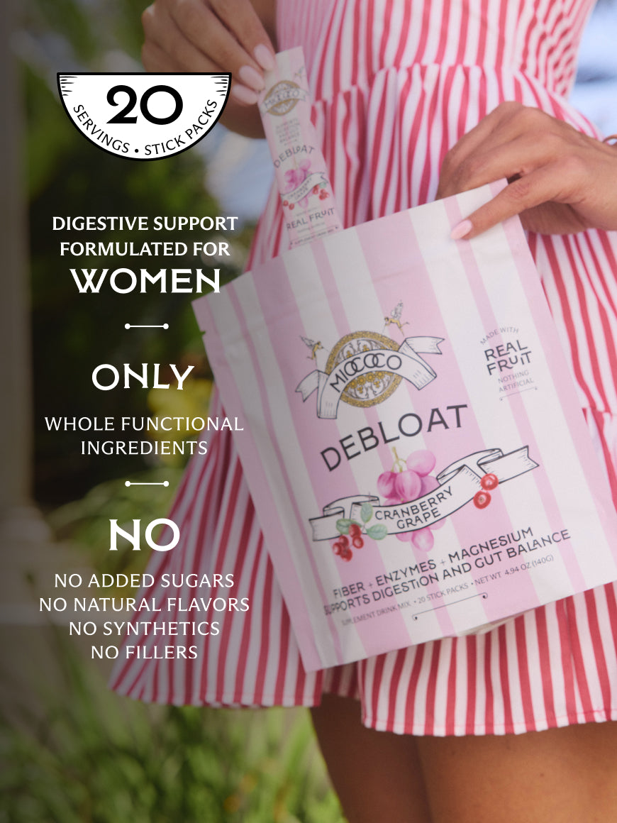 A person in a pink and white striped dress holds a bag of Debloat Cranberry Grape digestive support. The image features promotional text on the left highlighting '20 Servings + Stick Packs' and benefits for women, set against a blurred outdoor background.