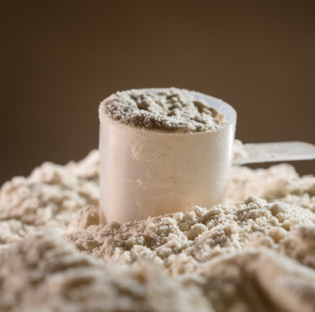 Protein scooper filled with protein powder on a bed of protein powder against a brown background.