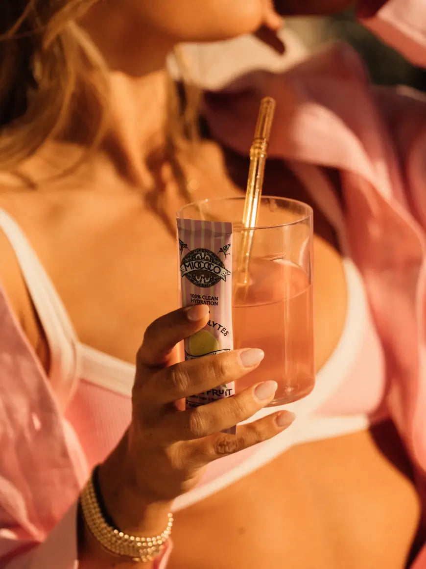 Person holding a glass of an electrolyte drink with a straw and a bottle, with a warm color tone.