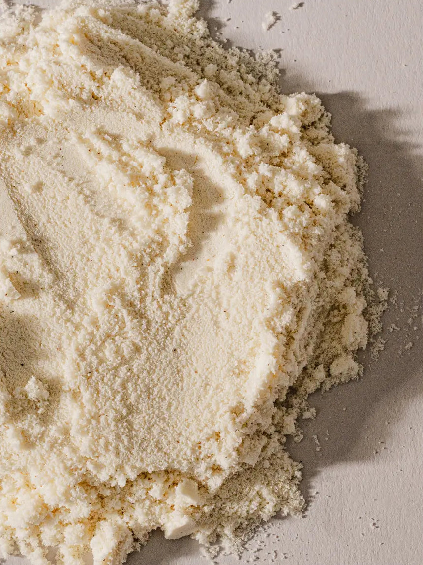 A close-up of a mound of vanilla whey protein isolate powder on a neutral light gray surface.